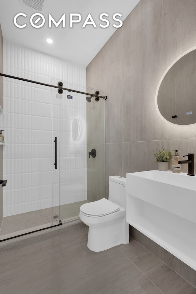 full bath featuring tile patterned flooring, toilet, a stall shower, tile walls, and a sink