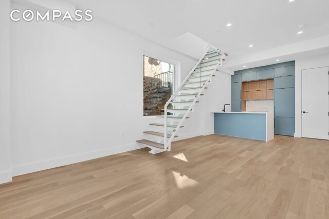 unfurnished living room featuring light wood finished floors, stairway, recessed lighting, and baseboards