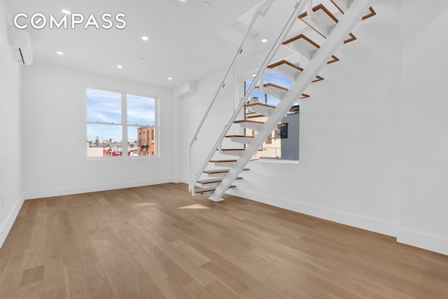 interior space featuring a wall unit AC, baseboards, stairway, and wood finished floors