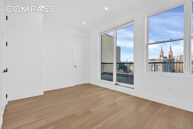 spare room featuring light wood finished floors, a view of city, baseboards, and recessed lighting