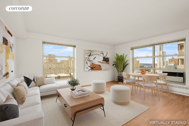 living room featuring visible vents, radiator heating unit, light wood-style flooring, a view of city, and a wealth of natural light