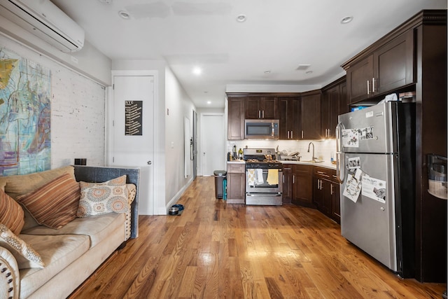 kitchen featuring dark brown cabinets, appliances with stainless steel finishes, a sink, an AC wall unit, and light wood-type flooring