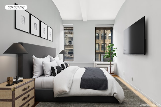 bedroom with beamed ceiling, baseboards, and wood finished floors