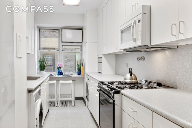 kitchen featuring white microwave, white cabinetry, black range with gas stovetop, decorative backsplash, and washer / clothes dryer