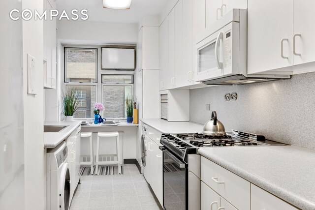 900 5th Ave Unit 14C, New York City, NY 10021 - kitchen featuring black gas stove, washer / clothes dryer, white microwave, backsplash, and white cabinets