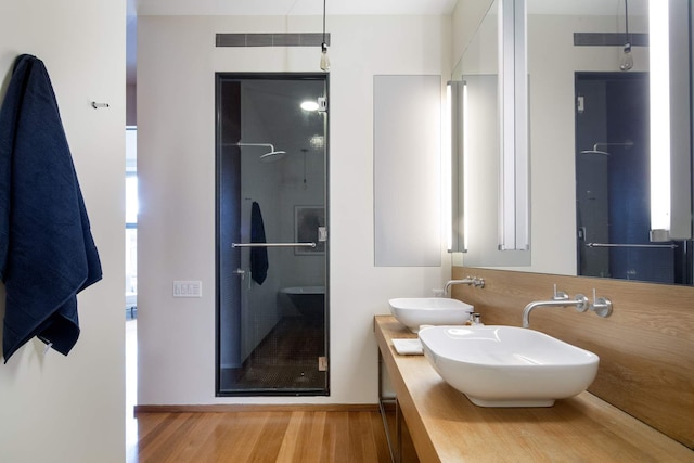 full bathroom with a stall shower, double vanity, a sink, and wood finished floors