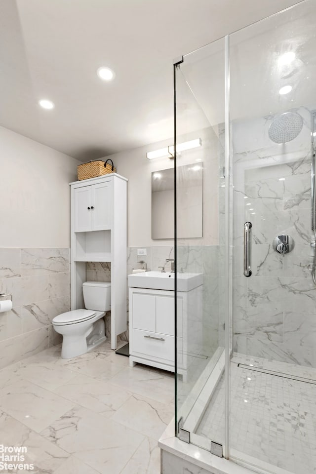 bathroom featuring tile walls, a wainscoted wall, vanity, toilet, and a marble finish shower