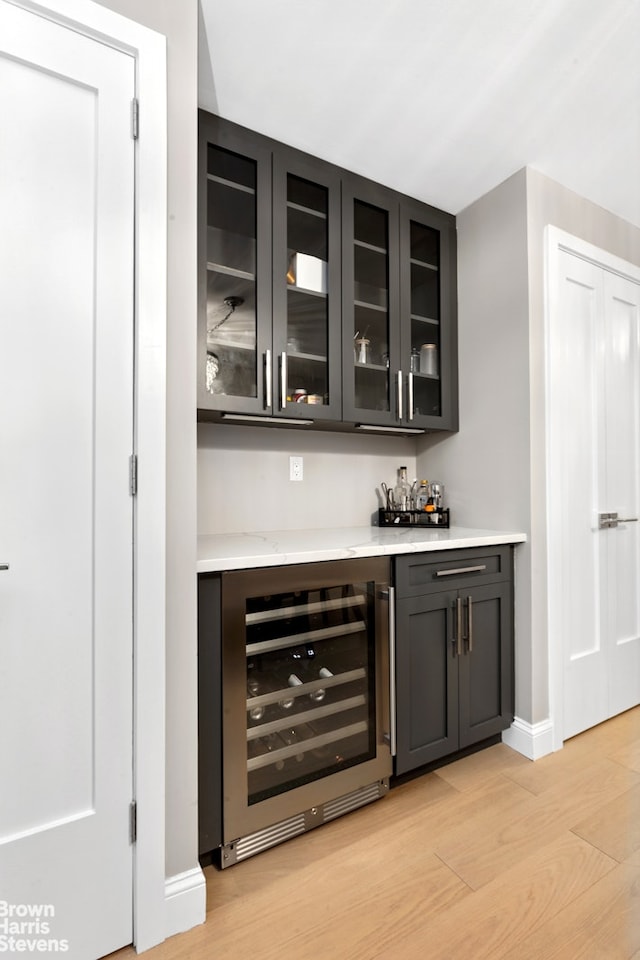 bar with wine cooler, baseboards, a dry bar, and light wood-type flooring