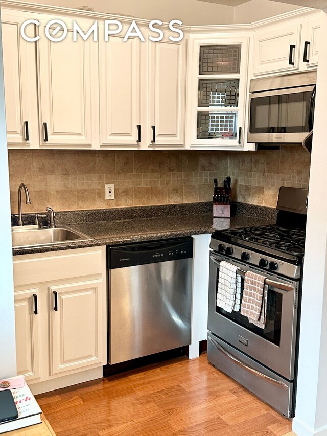 kitchen featuring light wood-type flooring, a sink, dark countertops, appliances with stainless steel finishes, and decorative backsplash