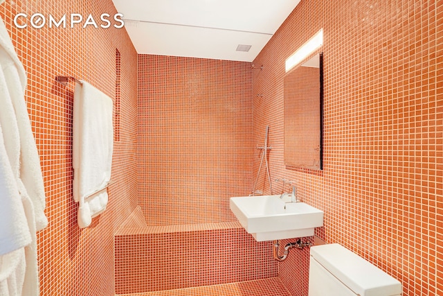 bathroom featuring toilet, tile walls, and a sink