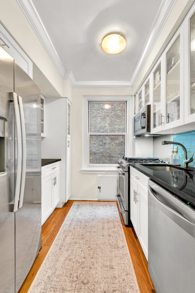 kitchen with crown molding, light wood finished floors, appliances with stainless steel finishes, glass insert cabinets, and white cabinetry