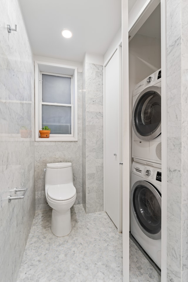 bathroom featuring stacked washer and clothes dryer, tile walls, and toilet