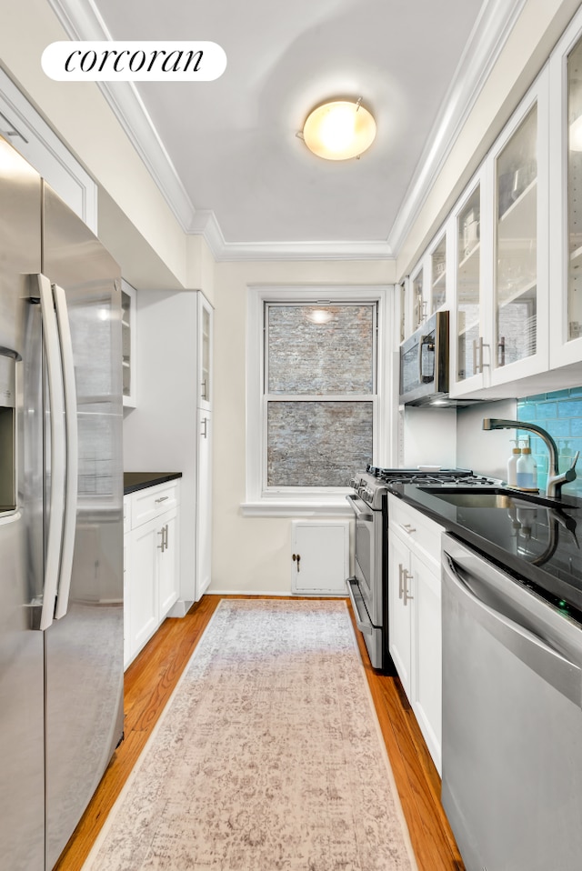 kitchen with light wood finished floors, dark countertops, appliances with stainless steel finishes, ornamental molding, and white cabinetry