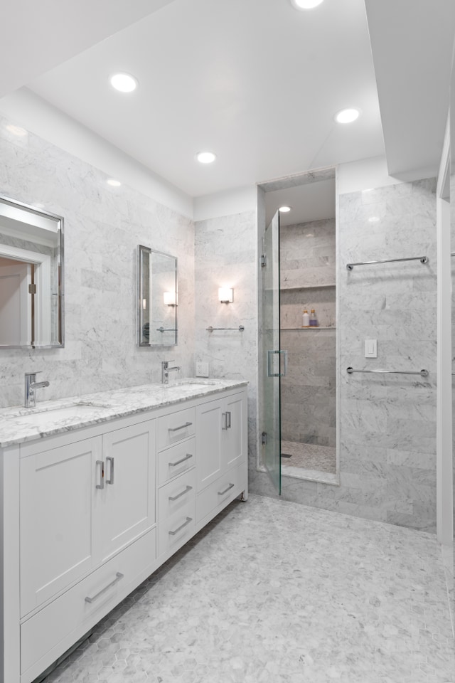 bathroom with tile walls, a sink, a shower stall, and double vanity