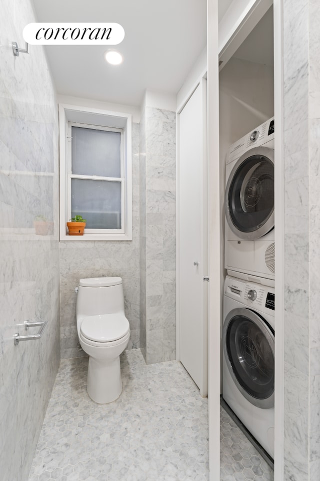 bathroom with toilet, tile walls, and stacked washer and clothes dryer