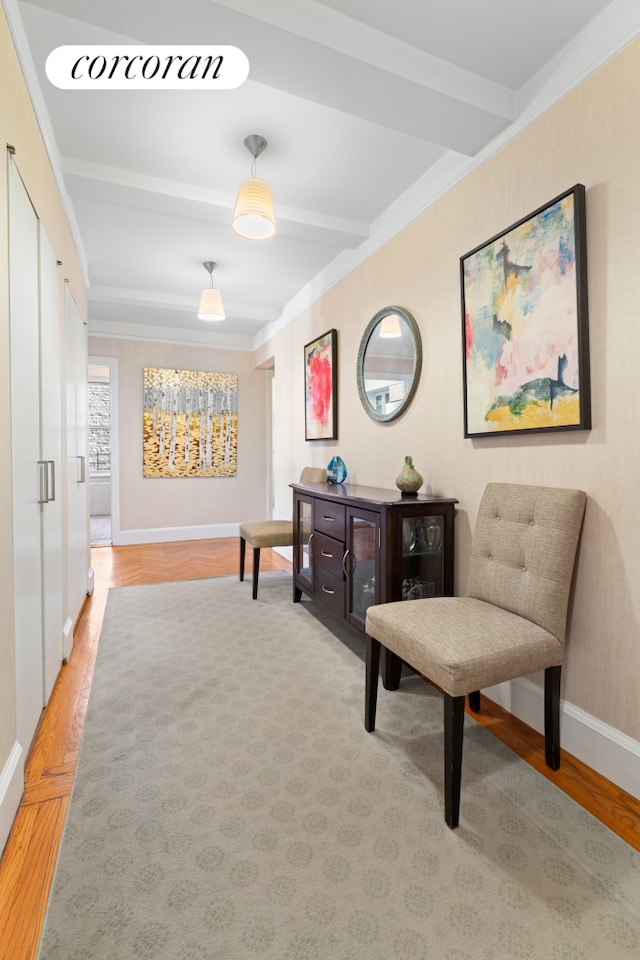 sitting room with light wood finished floors, baseboards, beamed ceiling, and ornamental molding