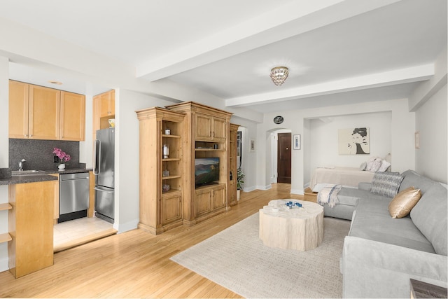 living room featuring beam ceiling, baseboards, arched walkways, and light wood-type flooring