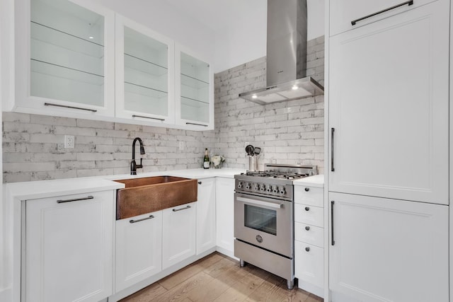 kitchen featuring white cabinets, a sink, high end stainless steel range oven, and wall chimney exhaust hood