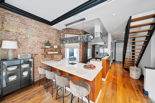 kitchen featuring island range hood, a sink, light wood finished floors, and brick wall