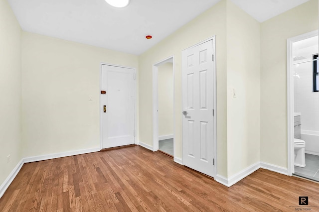 unfurnished bedroom with ensuite bath, wood finished floors, and baseboards