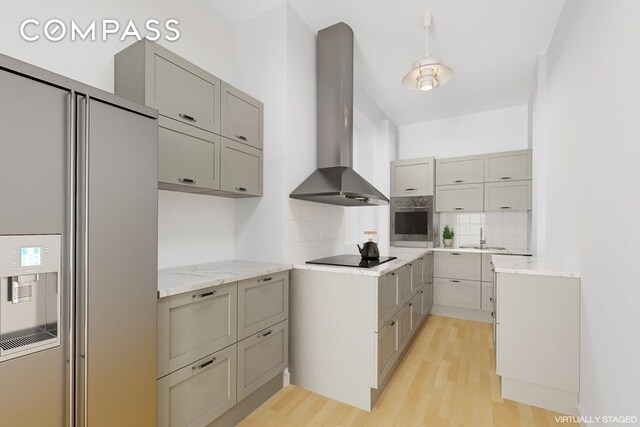 kitchen with wall chimney range hood, backsplash, refrigerator with ice dispenser, black electric stovetop, and oven