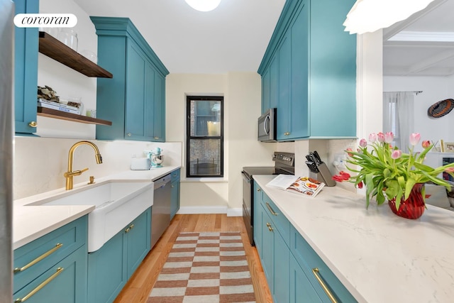 kitchen featuring light wood finished floors, stainless steel appliances, light countertops, blue cabinetry, and open shelves