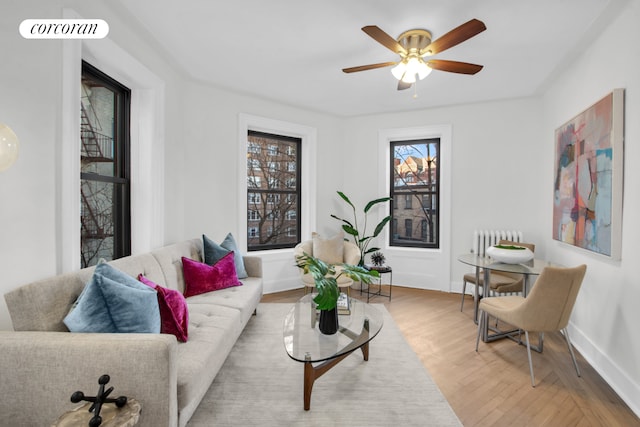 living room featuring visible vents, baseboards, a ceiling fan, light wood-style floors, and radiator heating unit