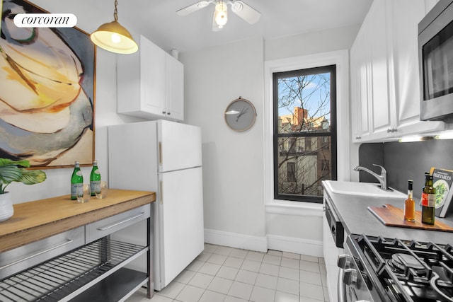 kitchen with light tile patterned floors, appliances with stainless steel finishes, white cabinetry, a sink, and baseboards