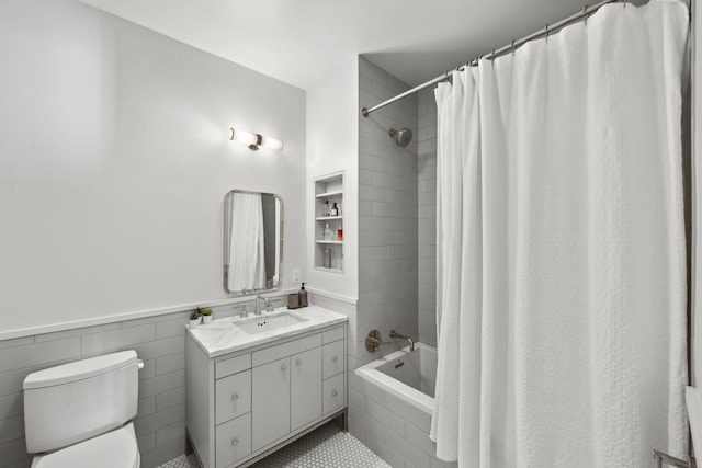 full bath featuring tile walls, tiled shower / bath, toilet, wainscoting, and vanity