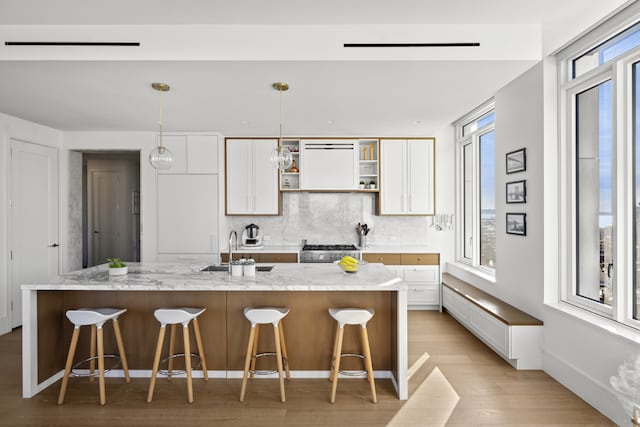 kitchen with open shelves, tasteful backsplash, light wood-style floors, stainless steel gas stove, and white cabinetry