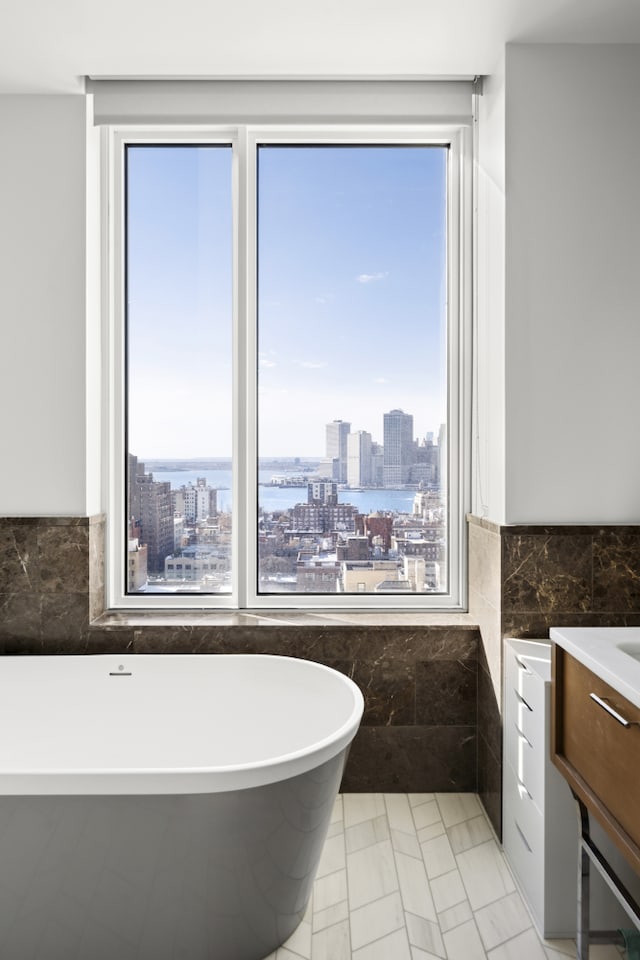 full bathroom featuring a city view, a wainscoted wall, vanity, tile walls, and a freestanding bath