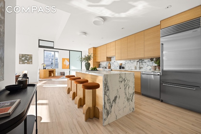 kitchen with a center island, tasteful backsplash, light wood-style flooring, appliances with stainless steel finishes, and light brown cabinets