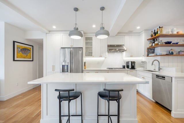 kitchen featuring a breakfast bar area, extractor fan, light wood-style flooring, stainless steel appliances, and a sink