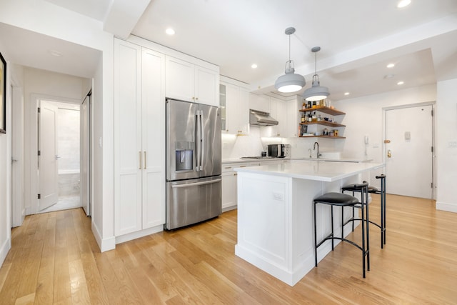 kitchen with light wood finished floors, stainless steel fridge, white cabinets, under cabinet range hood, and open shelves