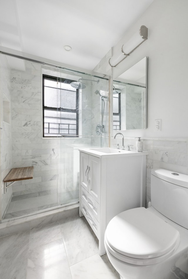 bathroom featuring toilet, marble finish floor, vanity, a shower stall, and tile walls