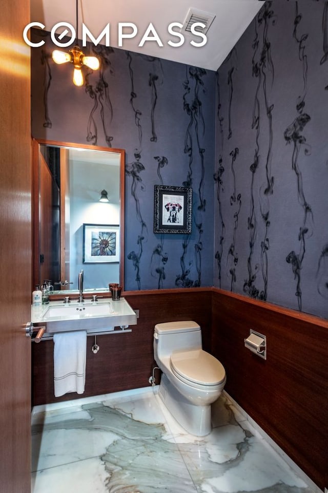 half bathroom with a sink, toilet, and marble finish floor