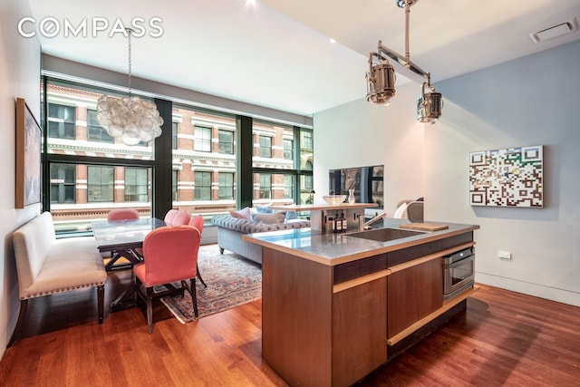 kitchen featuring dark wood finished floors, a sink, stainless steel counters, wall oven, and a chandelier