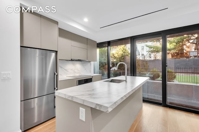 kitchen featuring light wood finished floors, stainless steel fridge, tasteful backsplash, gray cabinetry, and a sink