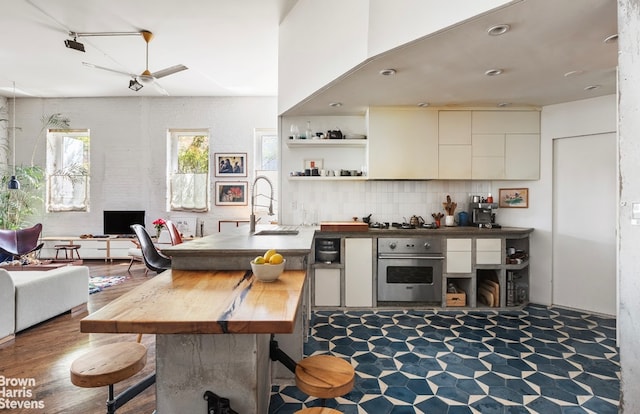 kitchen featuring open shelves, tasteful backsplash, open floor plan, a sink, and oven