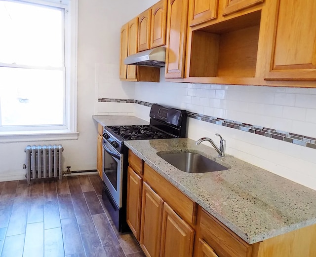 kitchen featuring under cabinet range hood, a sink, stainless steel gas range, decorative backsplash, and radiator heating unit