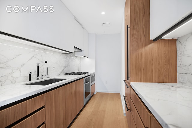 kitchen with light stone countertops, decorative backsplash, white cabinets, stainless steel appliances, and a sink