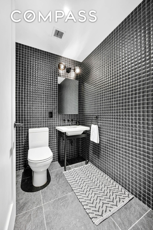 bathroom featuring toilet, visible vents, tile walls, and tile patterned floors