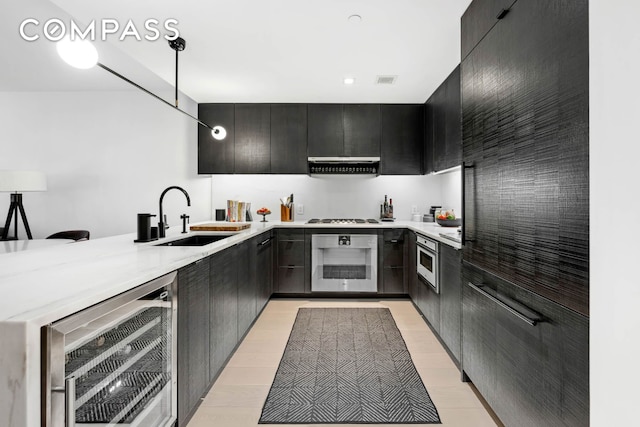 kitchen with cooktop, a sink, beverage cooler, oven, and under cabinet range hood