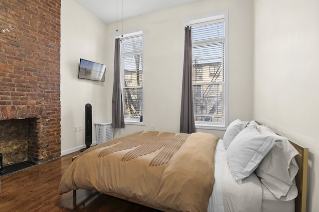 bedroom with a brick fireplace, wood finished floors, and baseboards