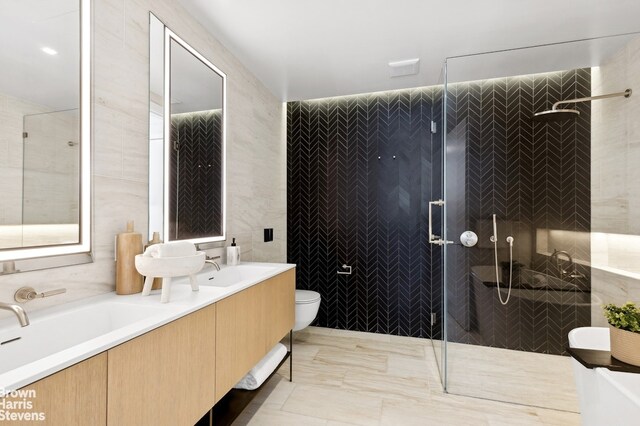 full bathroom with double vanity, tile walls, tiled shower, toilet, and a sink