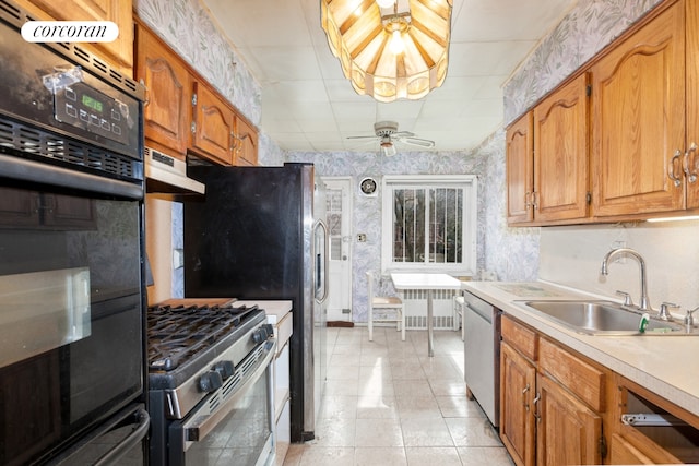 kitchen with ceiling fan, a sink, light countertops, appliances with stainless steel finishes, and wallpapered walls