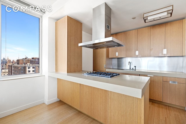 kitchen featuring light wood-style floors, stainless steel gas stovetop, a peninsula, and island range hood