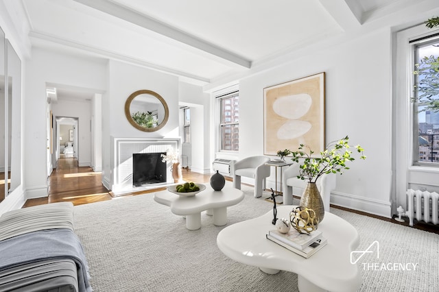 living area featuring baseboards, radiator heating unit, wood finished floors, a brick fireplace, and beam ceiling