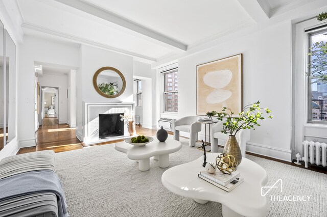 living area with radiator, wood finished floors, beamed ceiling, baseboards, and a brick fireplace