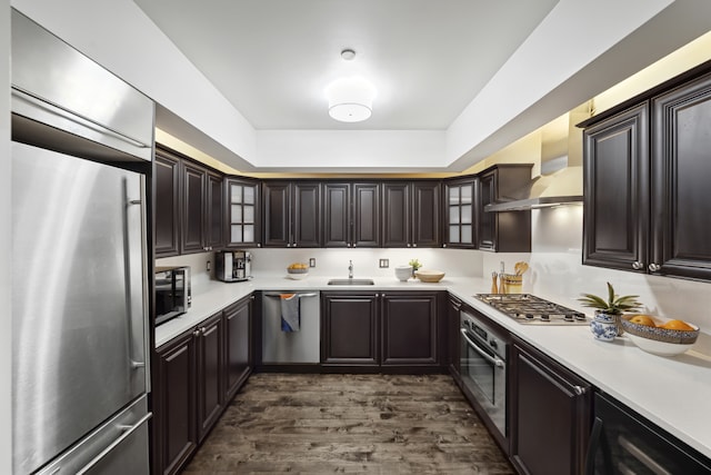 kitchen featuring stainless steel appliances, light countertops, dark brown cabinetry, a sink, and wall chimney exhaust hood